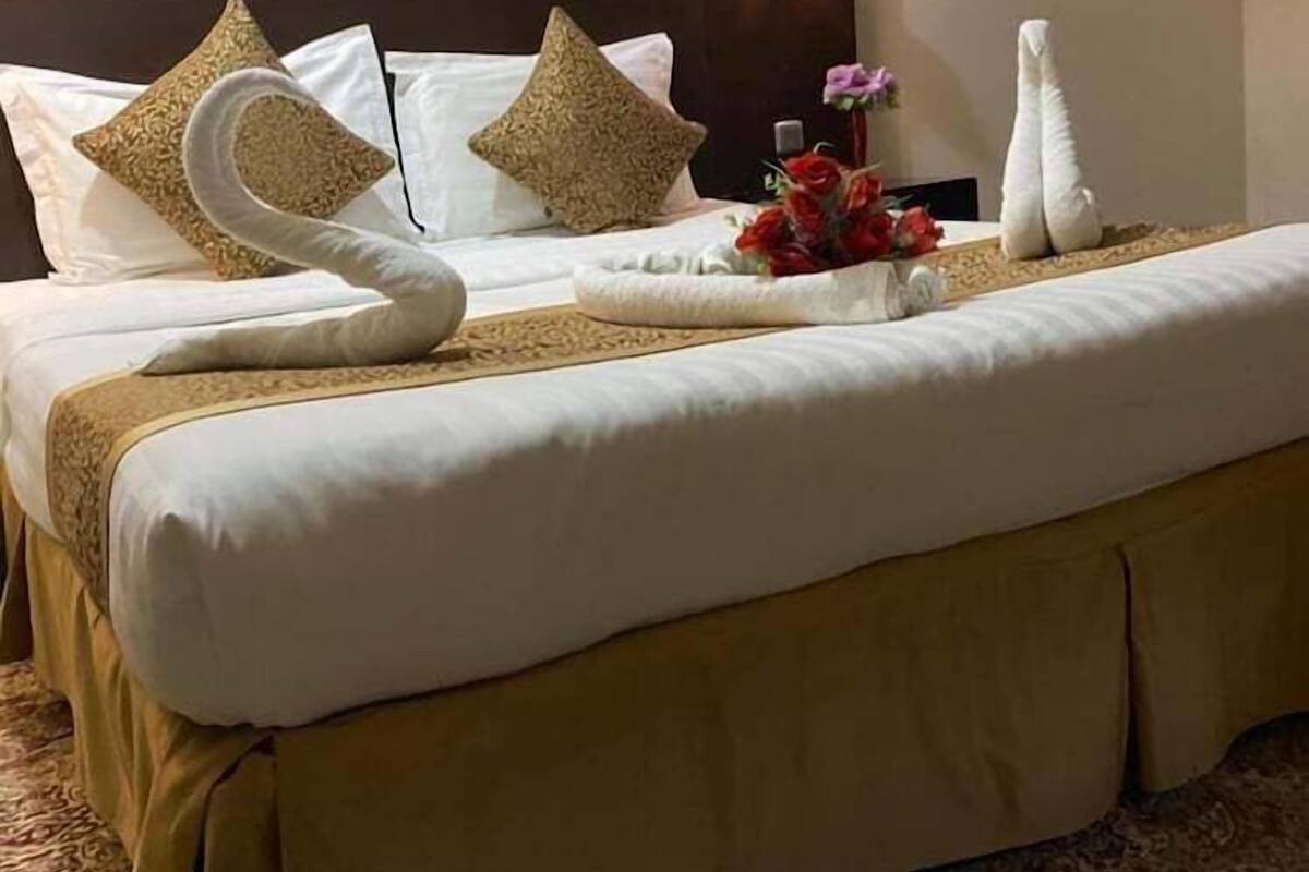 A hotel room with a large bed, a headboard, a bedside table with a lamp, and a framed picture on the wall.