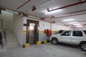 Un parking avec un VUS blanc stationné près d’une cage d’escalier et un extincteur fixé au mur.