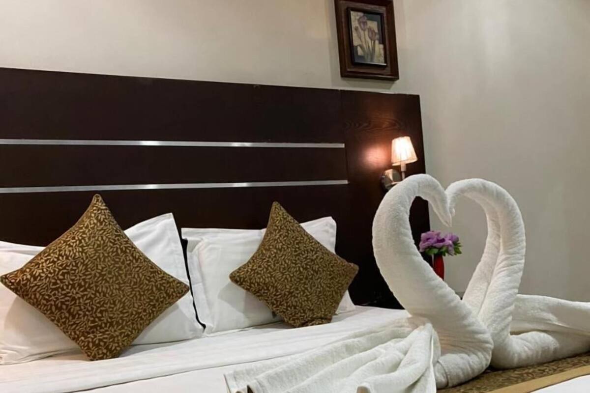 Un lit parfaitement fait, avec du linge de lit blanc, deux coussins décoratifs et une serviette pliée en forme de cygne.