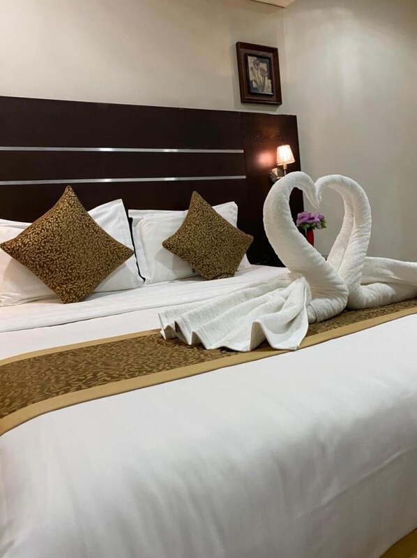 Un lit parfaitement fait, avec du linge de lit blanc, deux coussins décoratifs et une serviette pliée en forme de cygne.