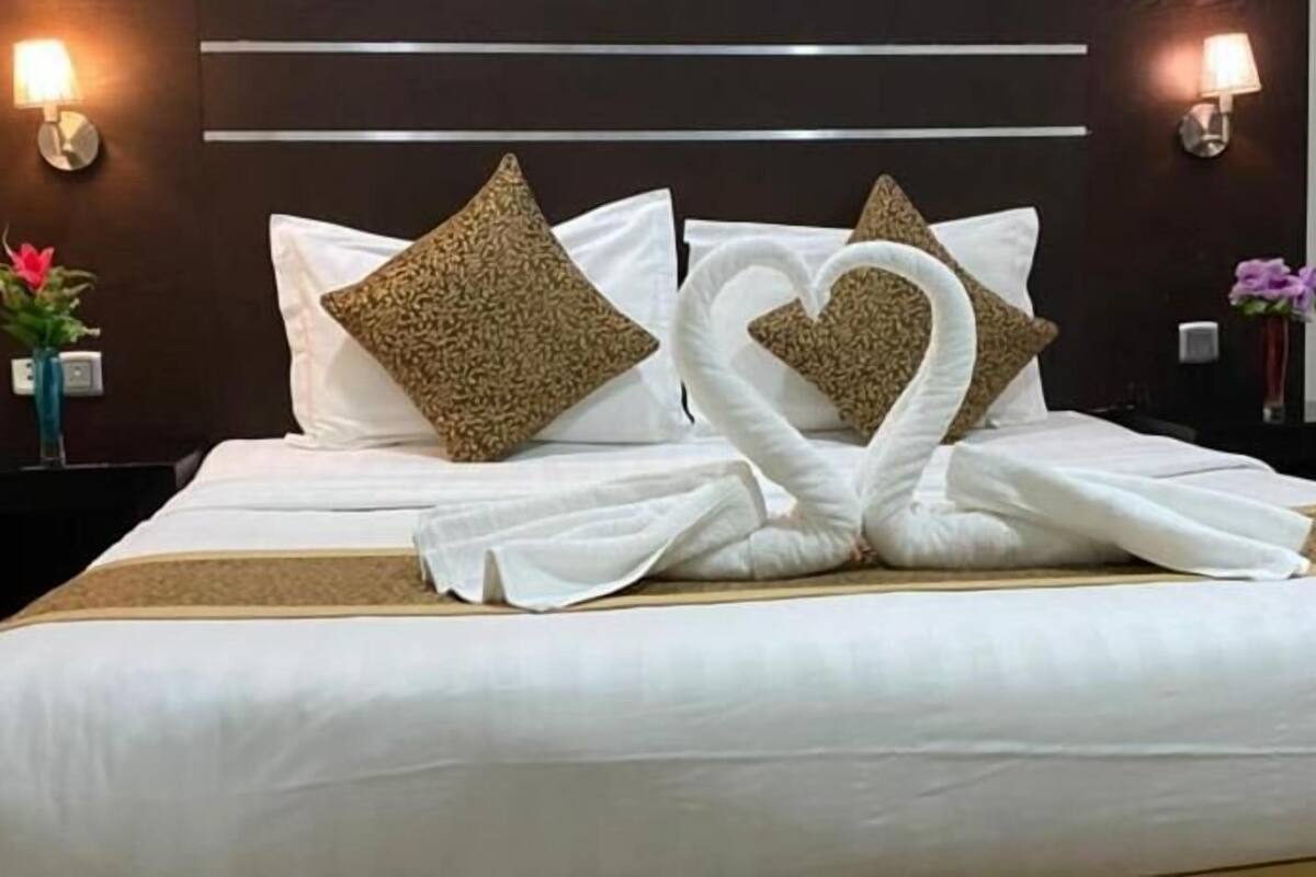 A hotel room with a neatly made bed, two wall-mounted lamps, and a vase with flowers on the nightstand.
