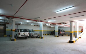 Un parking à plusieurs niveaux, avec plusieurs voitures garées, des piliers en béton et un éclairage au plafond.