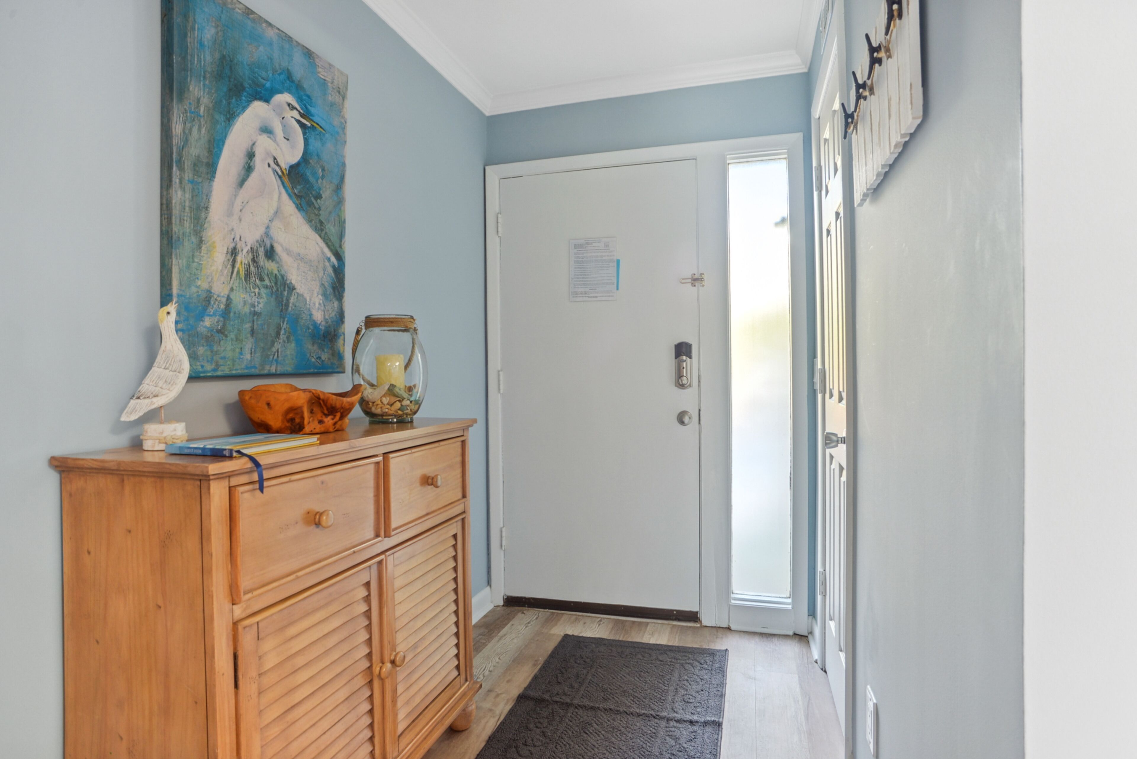 A hallway with a wooden cabinet, a painting of a bird, and a closed door.