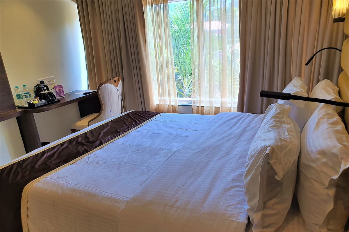 A hotel room with a large bed, a desk with a chair, and a window with curtains.