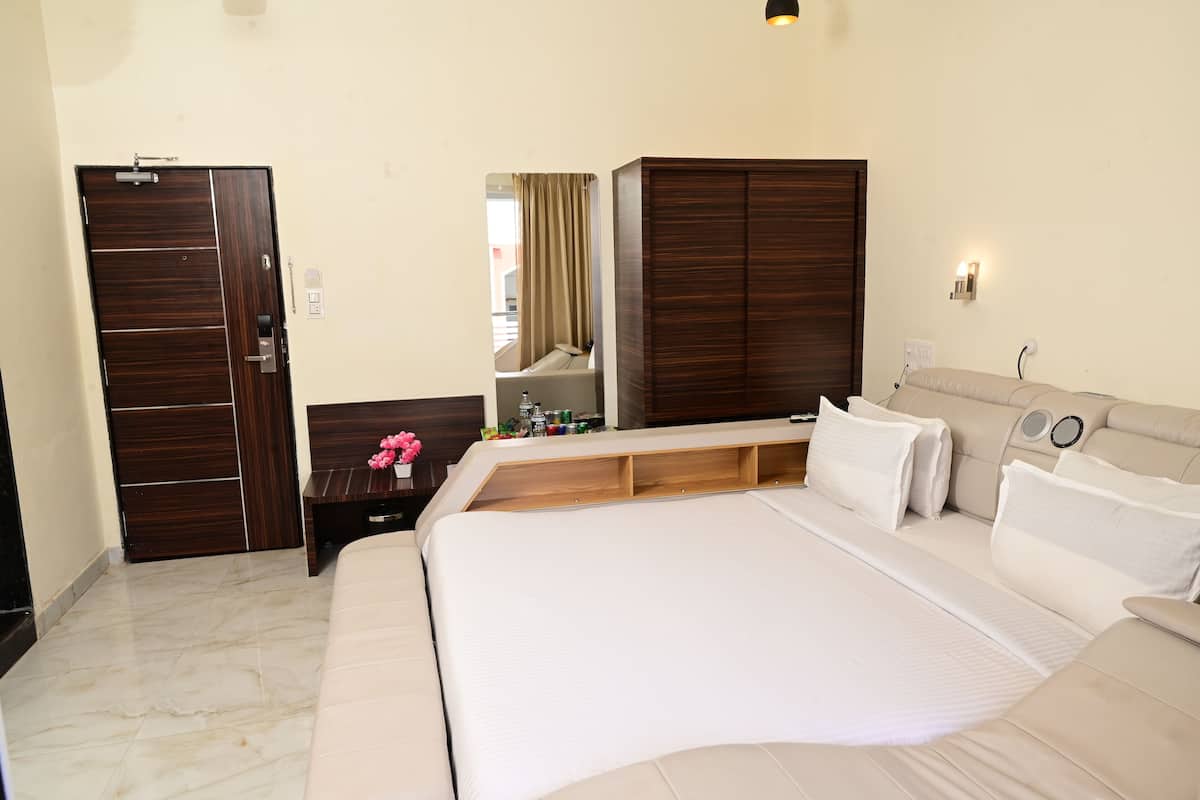 A hotel room with a large bed, a wooden wardrobe, a bedside table with a mirror, and a small desk.