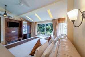 A hotel room with a bed, a sofa, a TV, a ceiling fan, and a window with curtains. - Shanti Solitaire Arpora (Arpora)