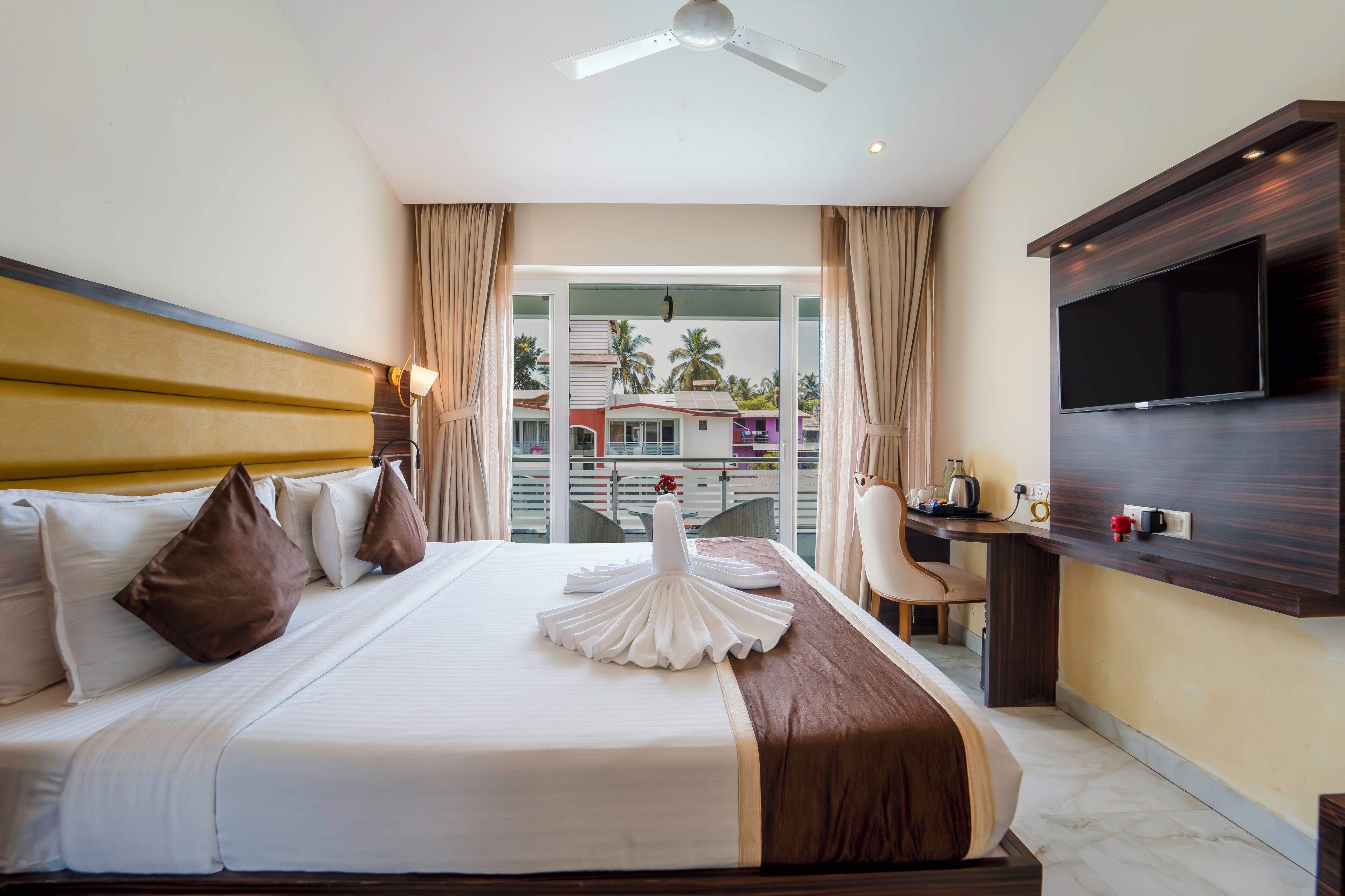 A hotel room with a bed, a desk, a television, and a view of palm trees.