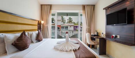 A hotel room with a bed, a desk, a television, and a view of palm trees.