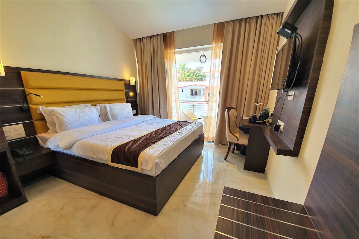 A hotel room with a large bed, a desk, a chair, a TV, and a view of the outside.