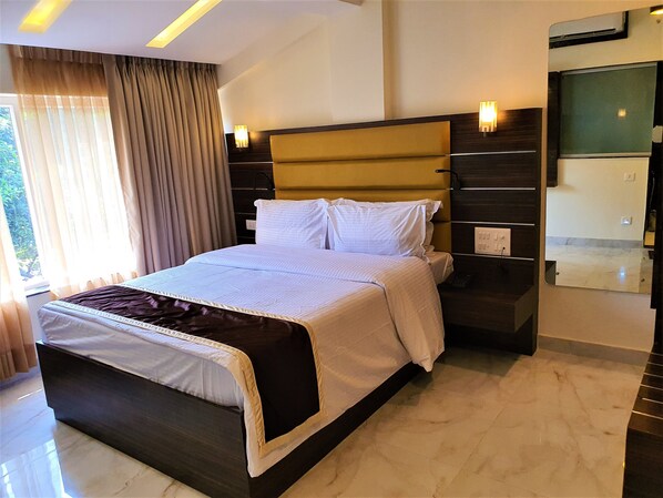A modern hotel room with a large bed, a headboard with integrated lighting, a bedside table, and a large mirror. - Ginger Arpora Goa (Arpora)