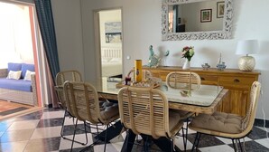 A dining area with a glass table, wicker chairs, a wooden cabinet, and a decorative mirror.