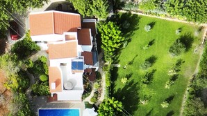 Eine Vogelperspektive eines Wohnhauses mit Swimmingpool, großem Garten und einem roten Auto vor der Einfahrt.