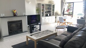 Ein Wohnzimmer mit Kamin, Fernseher, einer Couch und einem Essbereich mit Stühlen und Tisch.