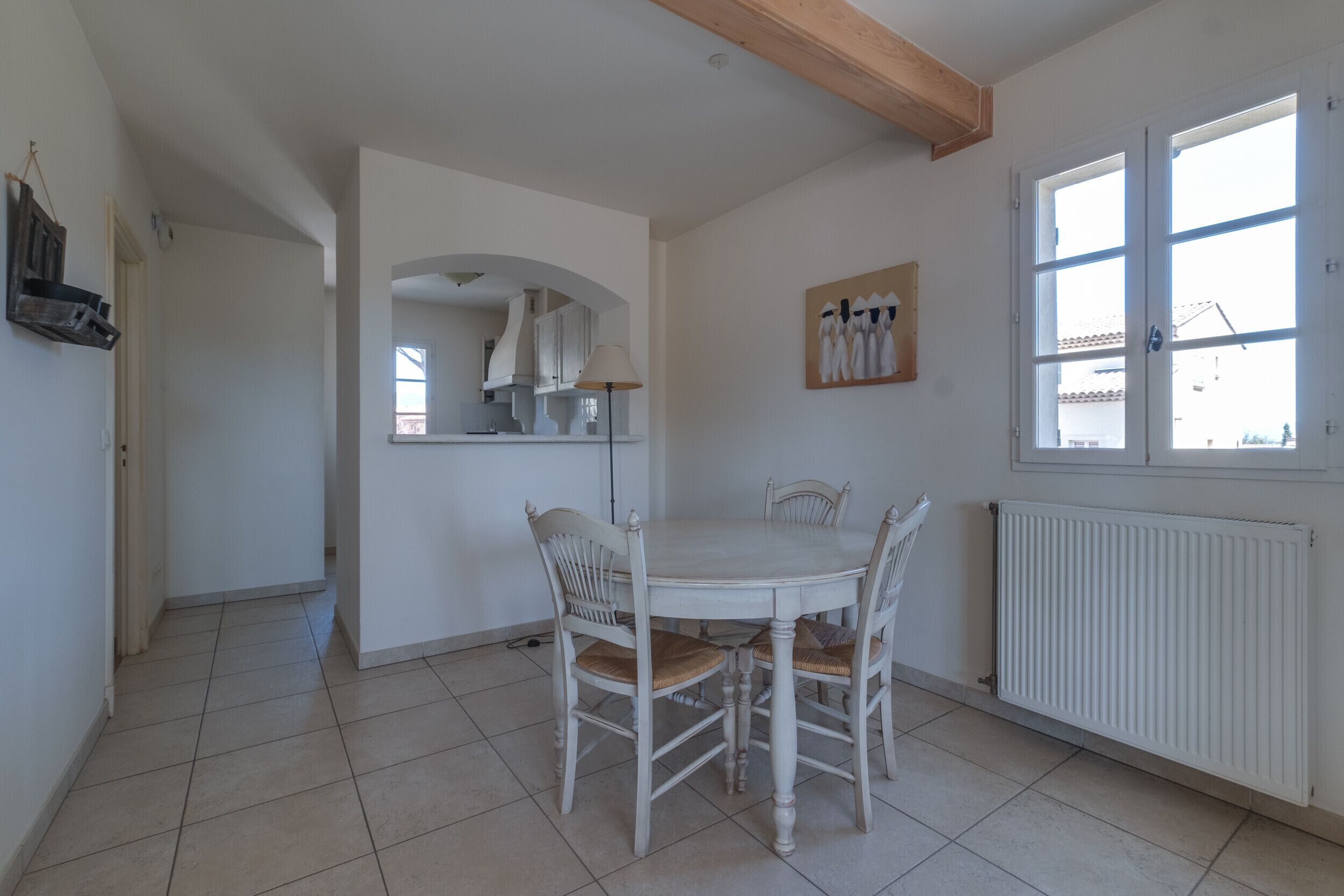 Een eetruimte met een ronde tafel en vier stoelen, een raam met zonwering en een radiator aan de muur.