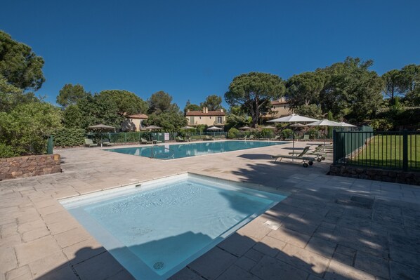 A swimming pool with a diving board, surrounded by a stone patio and greenery.