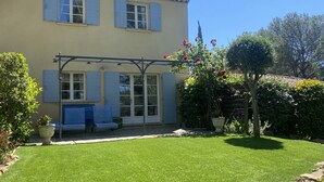 Une maison à deux étages dotée d’un patio couvert, d’une pelouse et d’un jardin agrémenté de plantes à fleurs.
