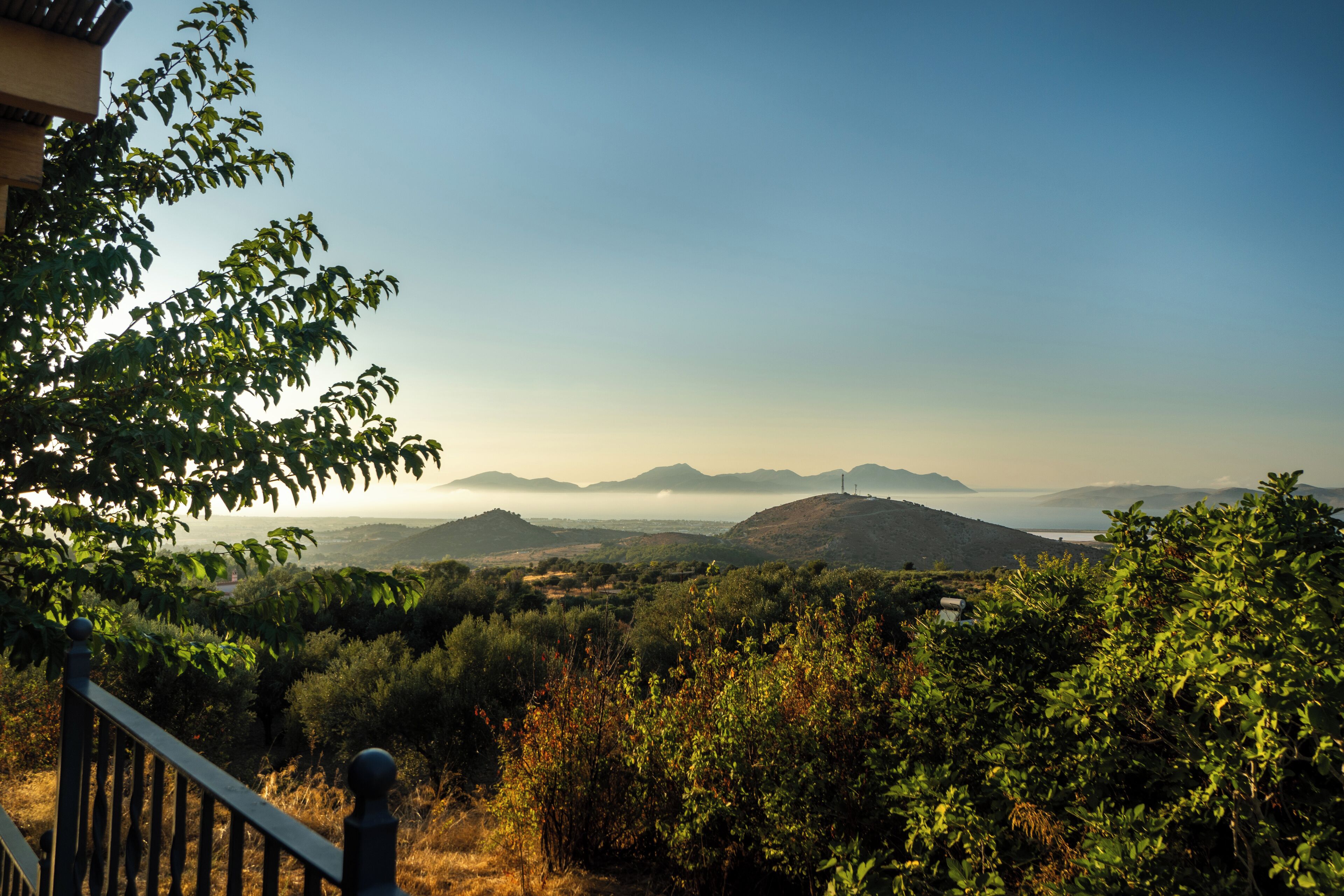 Vista d'un paisatge montanyós amb cel serè, una massa d'aigua a la distància i vegetació abundant.