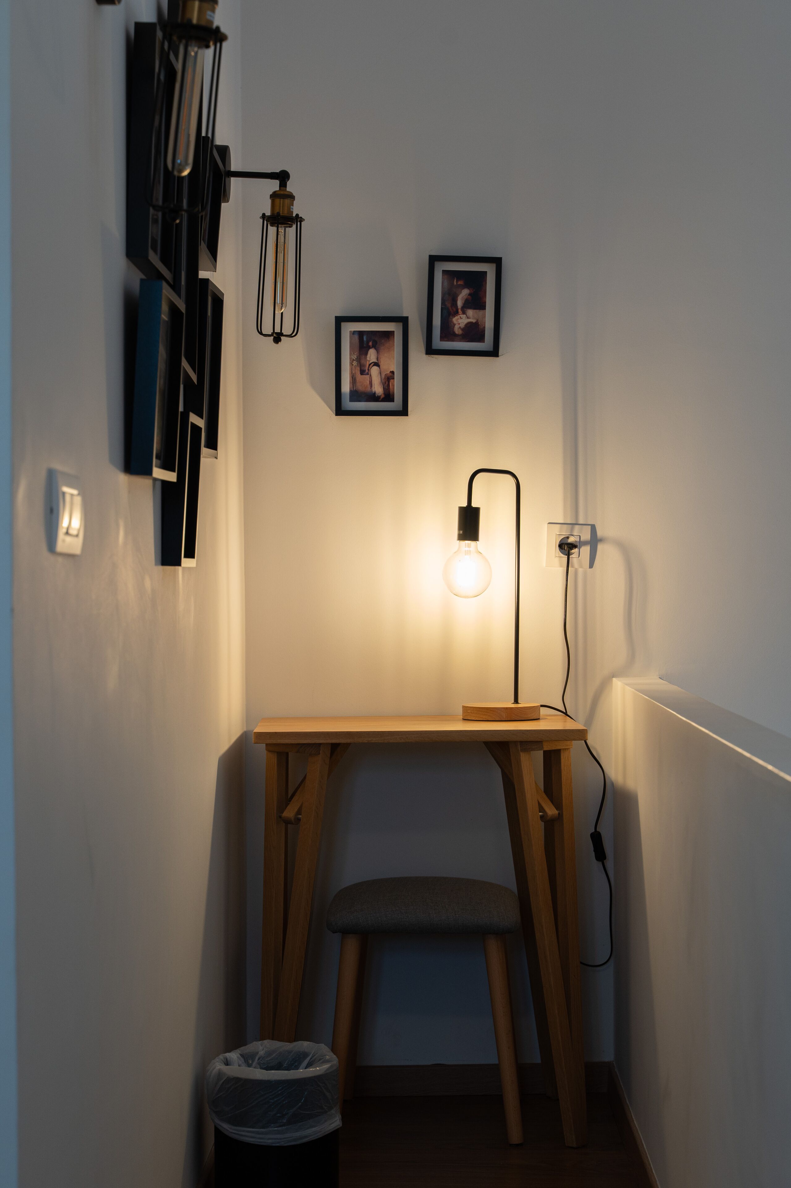 Habitación de esquina con un escritorio de madera, una banca, un cesto de basura y cuadros colgados en la pared.
