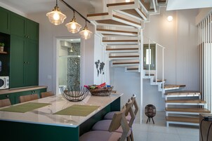 Una cocina moderna con una isla central, armarios verdes y una escalera de madera.