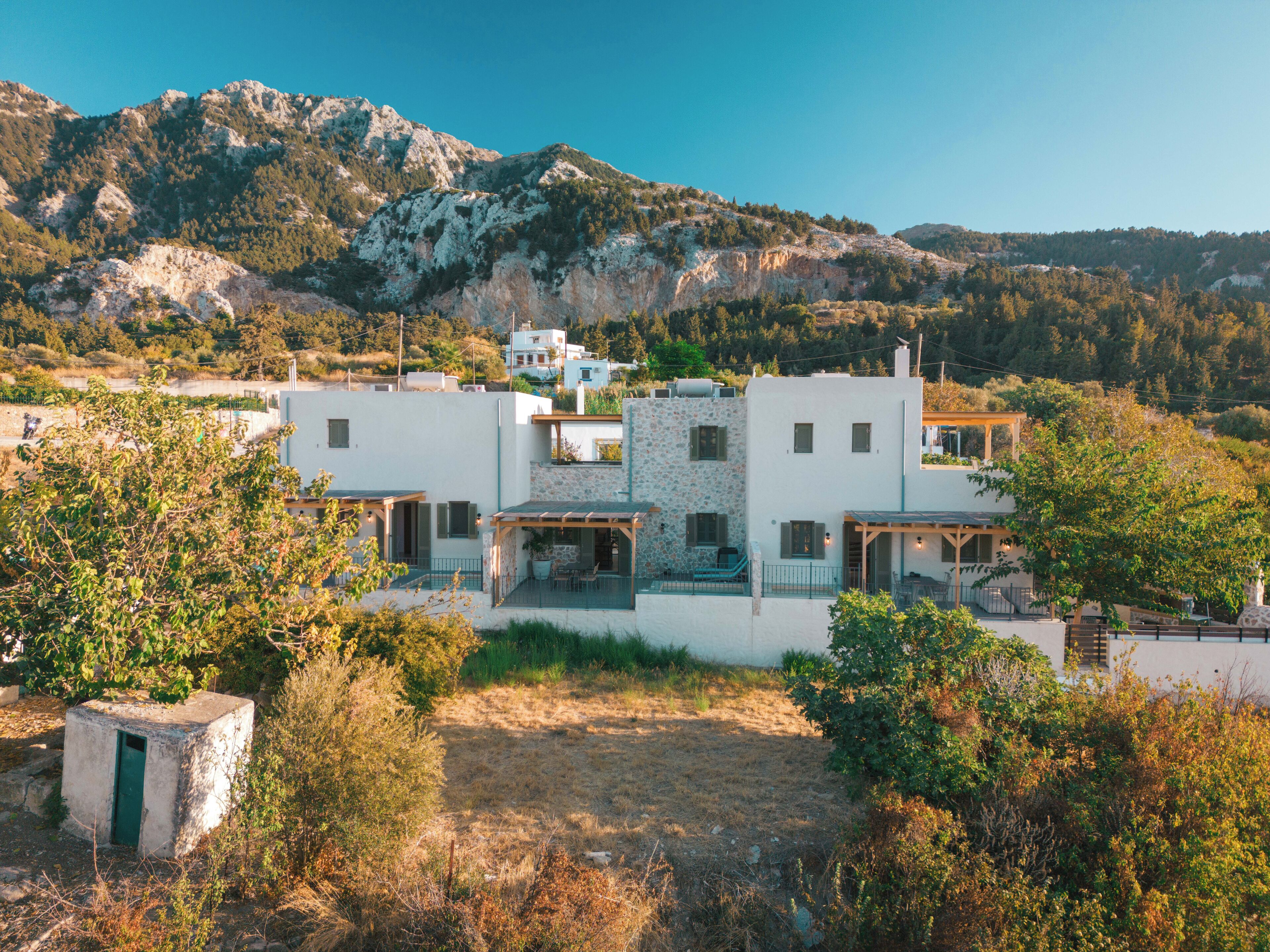 Una casa moderna de dos pisos con fachada de piedra, varios balcones y vistas del paisaje montañoso circundante.
