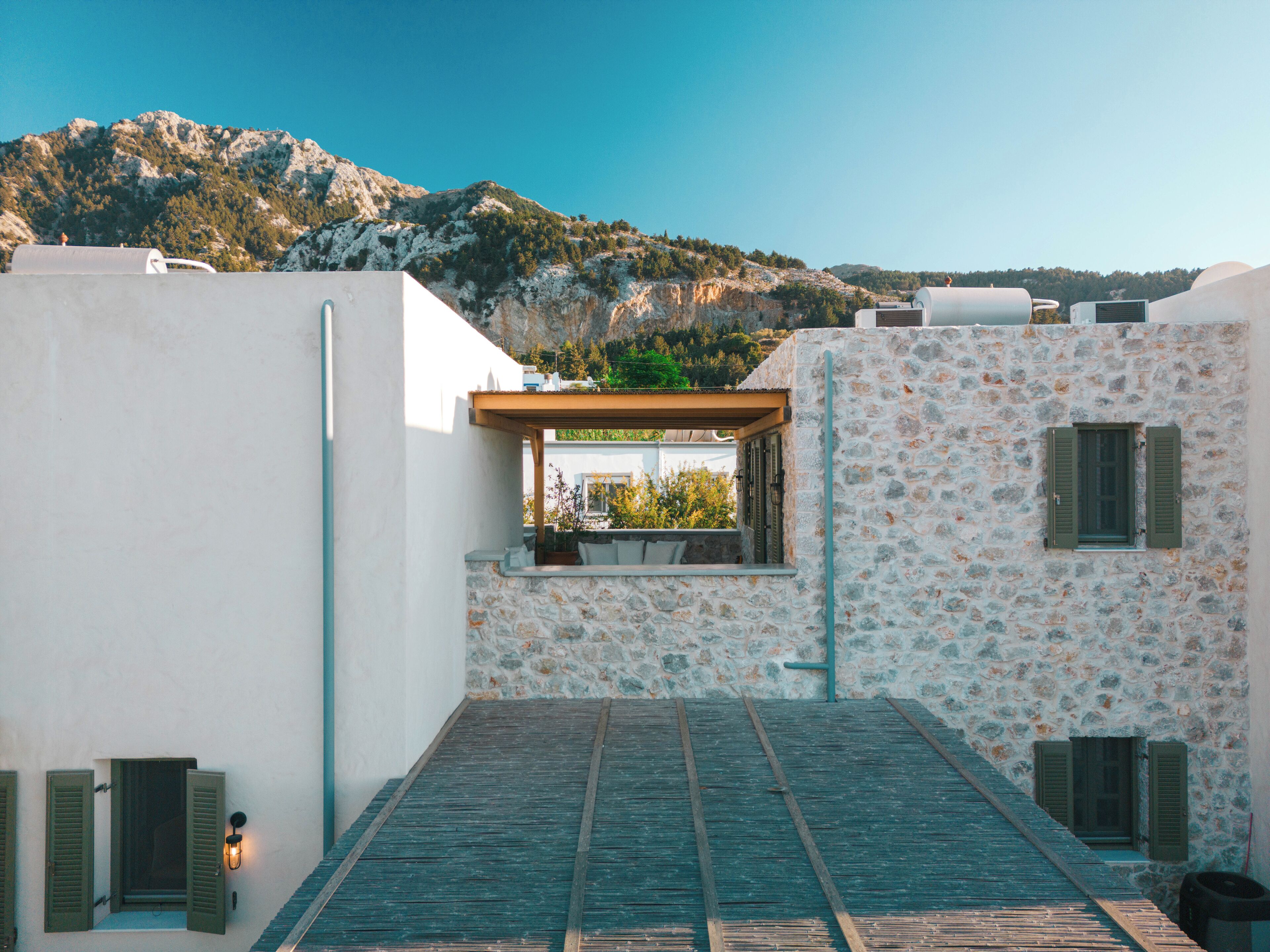 A rooftop terrace with a stone wall, a wooden deck, and a view of a mountainous landscape.