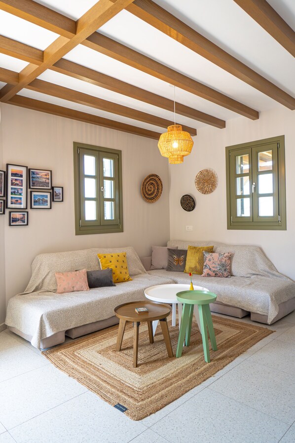 A cozy living room with a sofa, a small table, and a hanging light fixture. - Villa Rosa - Luxury Villas with Panoramic Views (Kos)