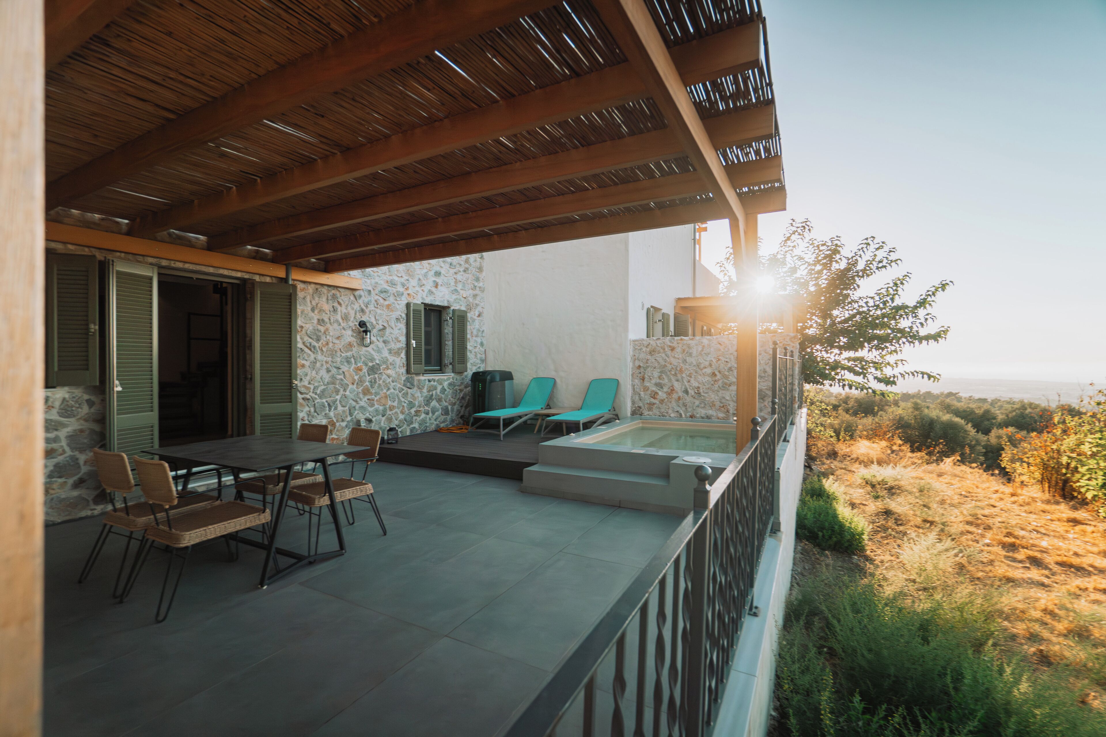 Eine überdachte Terrasse im Freien mit Steinmauer, Pool und Liegestühlen.