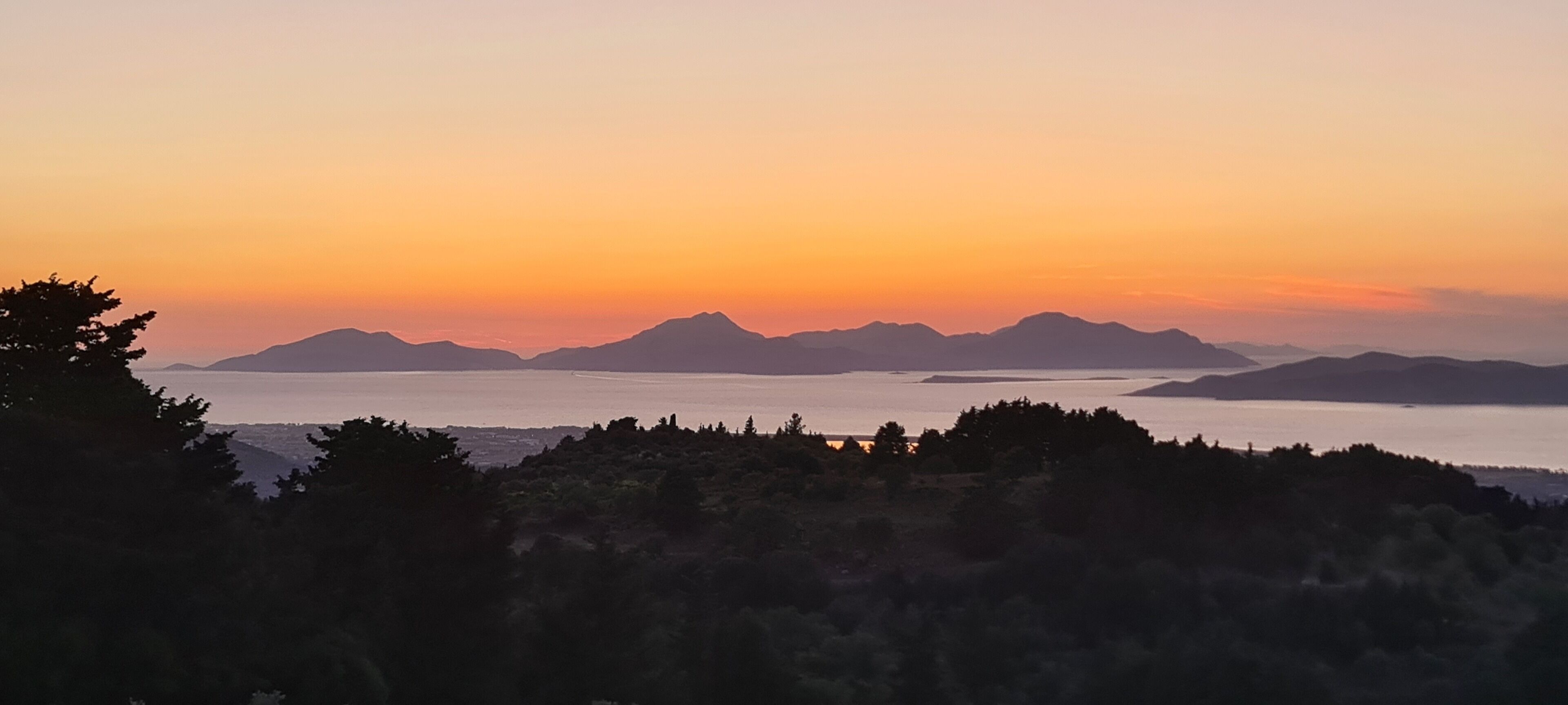 Un paysage côtier avec des montagnes et une étendue d’eau au coucher du soleil.