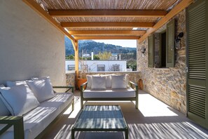 A balcony with a wooden pergola, a white sofa with cushions, a metal table, and a stone wall.