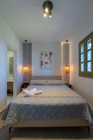 A bedroom with a bed, bedside tables, a hanging light fixture, a window, and a painting on the wall.