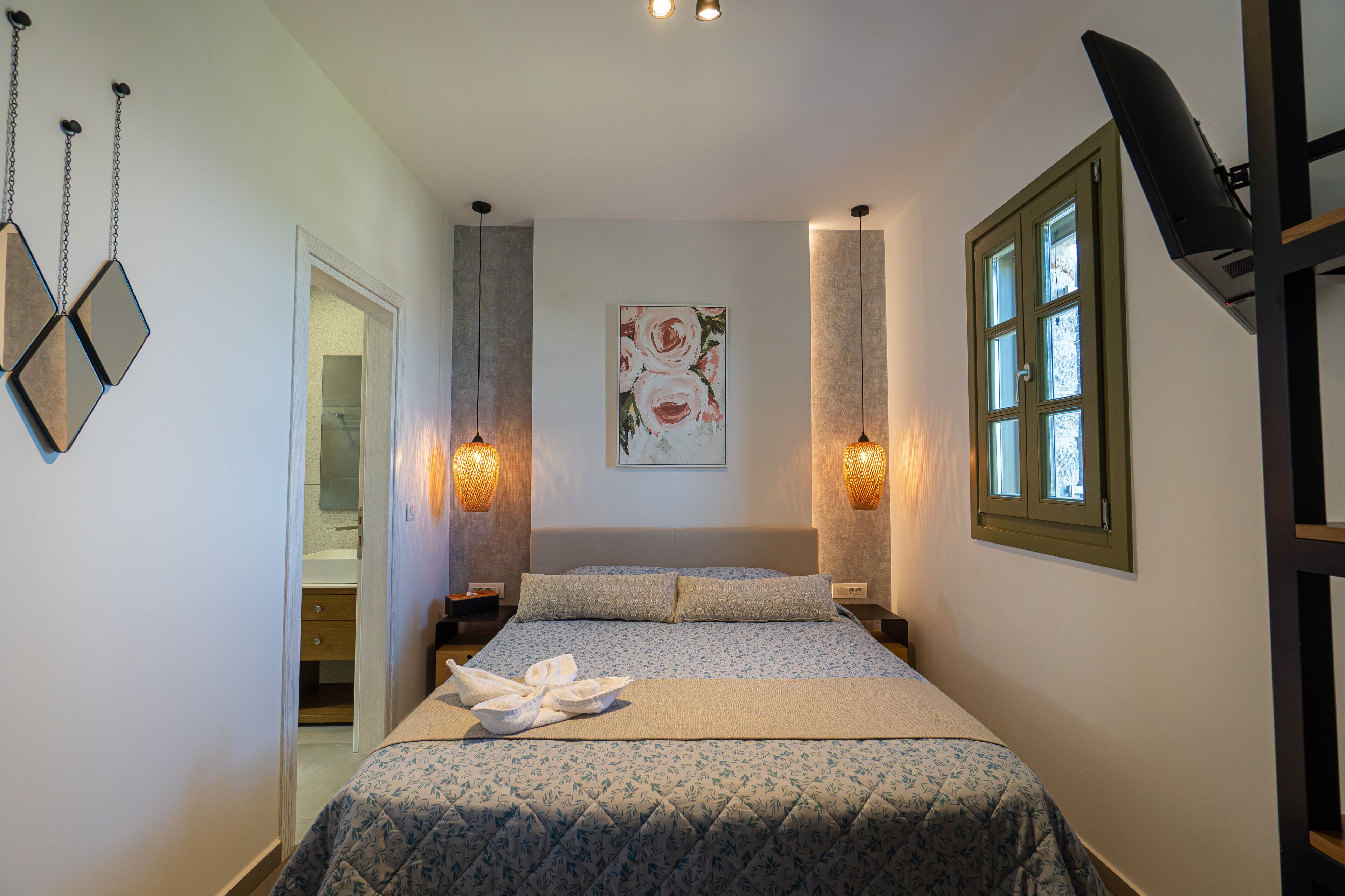 A neatly made bed with a floral bedspread, two bedside lamps, a painting on the wall, and a window with blinds.