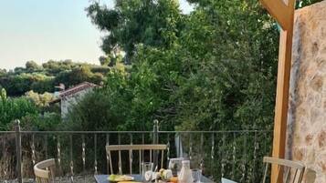 An outdoor dining area with a table set for two, surrounded by wicker chairs, under a wooden pergola.