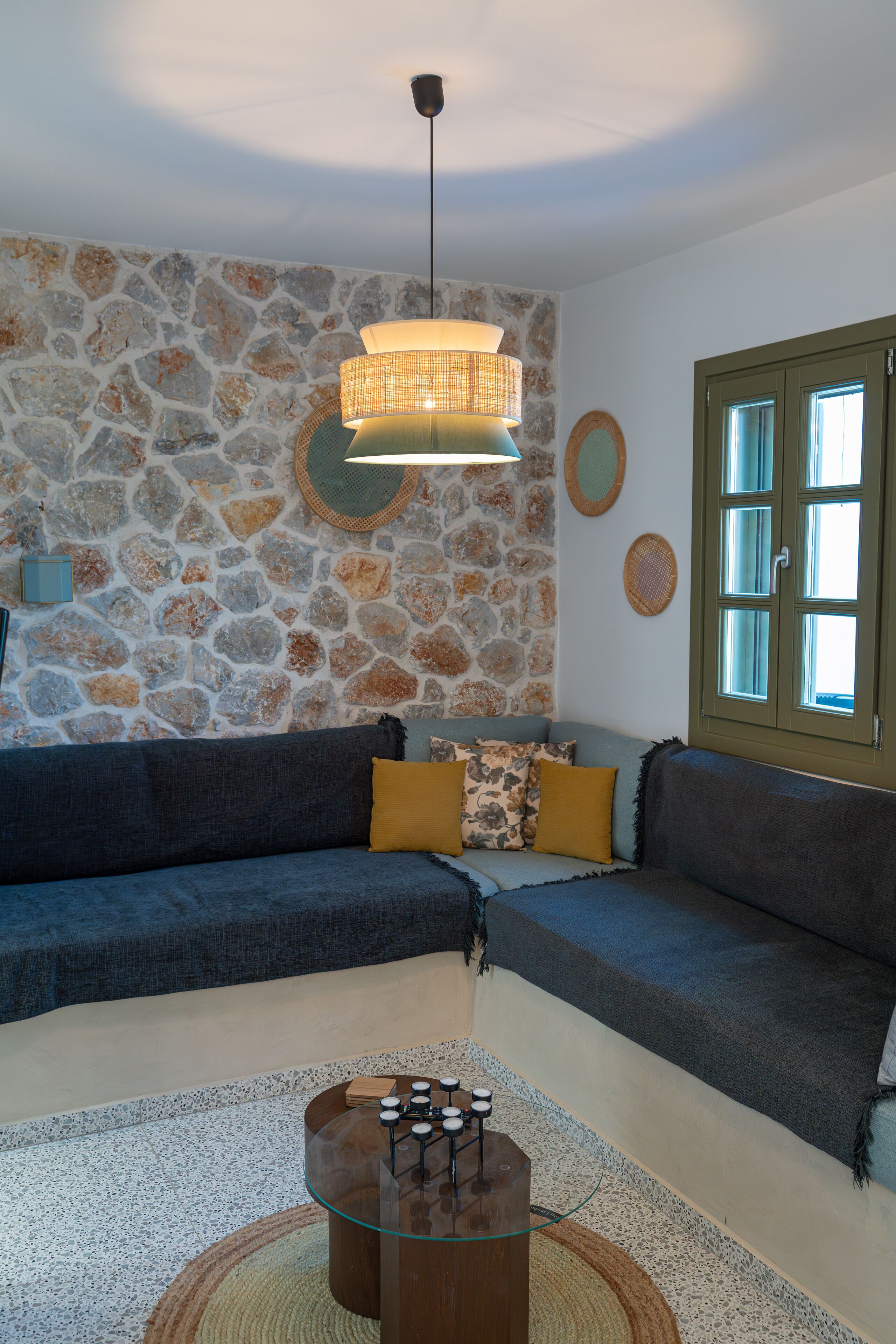 A living room with a stone wall, a sofa, a glass coffee table, and a hanging light fixture.