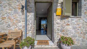 A stone building entrance with a wooden bench, a doormat, and potted plants.