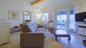 A living room with a sofa, dining table, chairs, and a television. - 2 BEDROOM TOWNHOUSE WITH GARDEN (N°507) (La Motte)