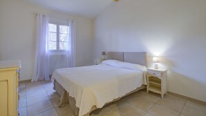 A bedroom with a bed, a nightstand, a window with curtains, and a radiator. - 2 BEDROOM TOWNHOUSE WITH GARDEN (N°507) (La Motte)