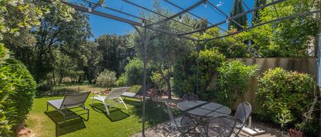Un patio con pérgola, mobiliario exterior y suelo de piedra.