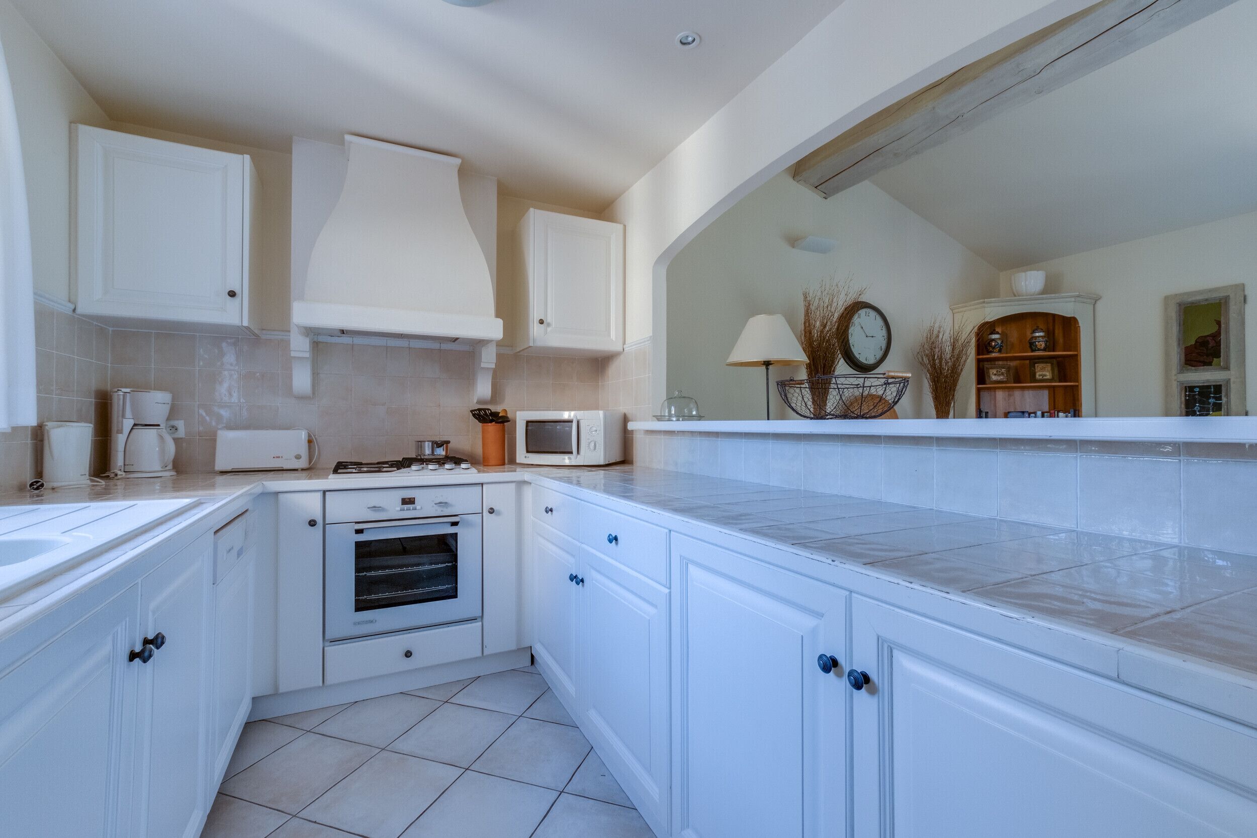 A modern kitchen with white cabinets, a built-in oven, a microwave, and a coffee maker.