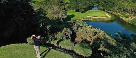 A golf course with a water body, trees, and a hilly landscape.