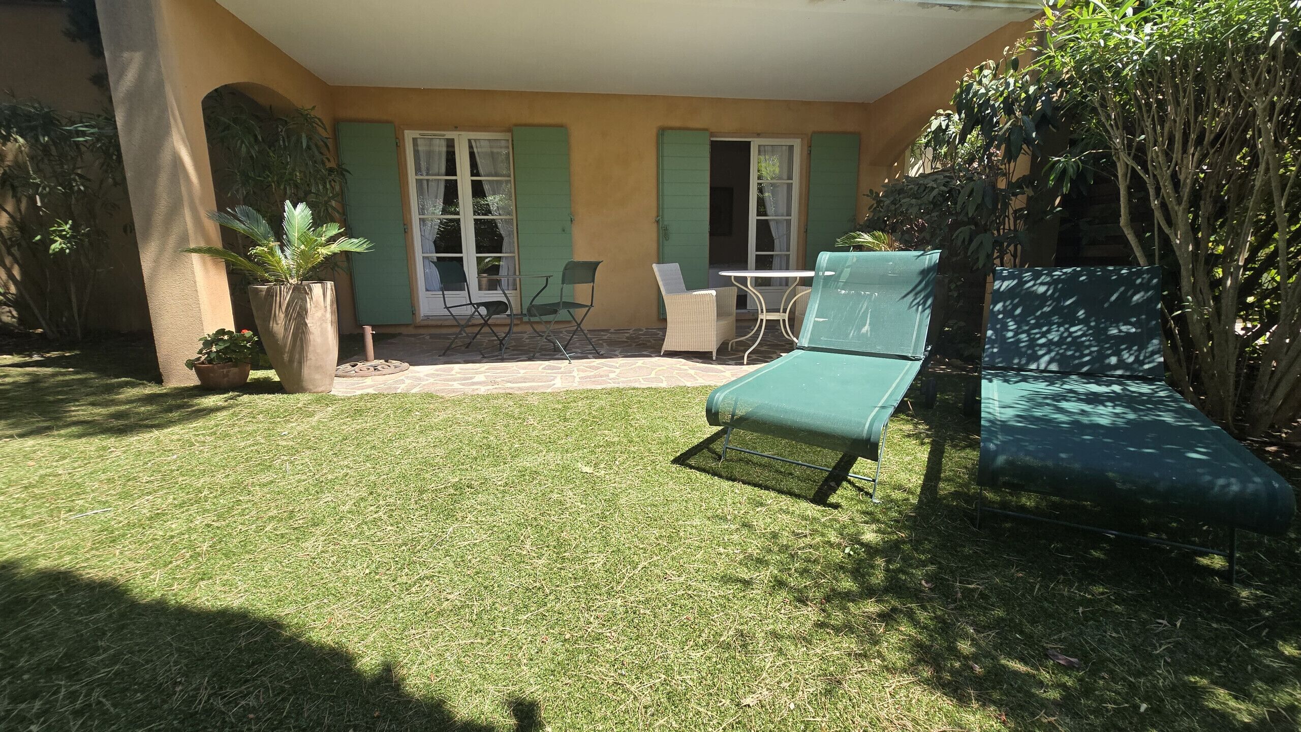 A patio with a lawn, a table, chairs, and a lounge chair.