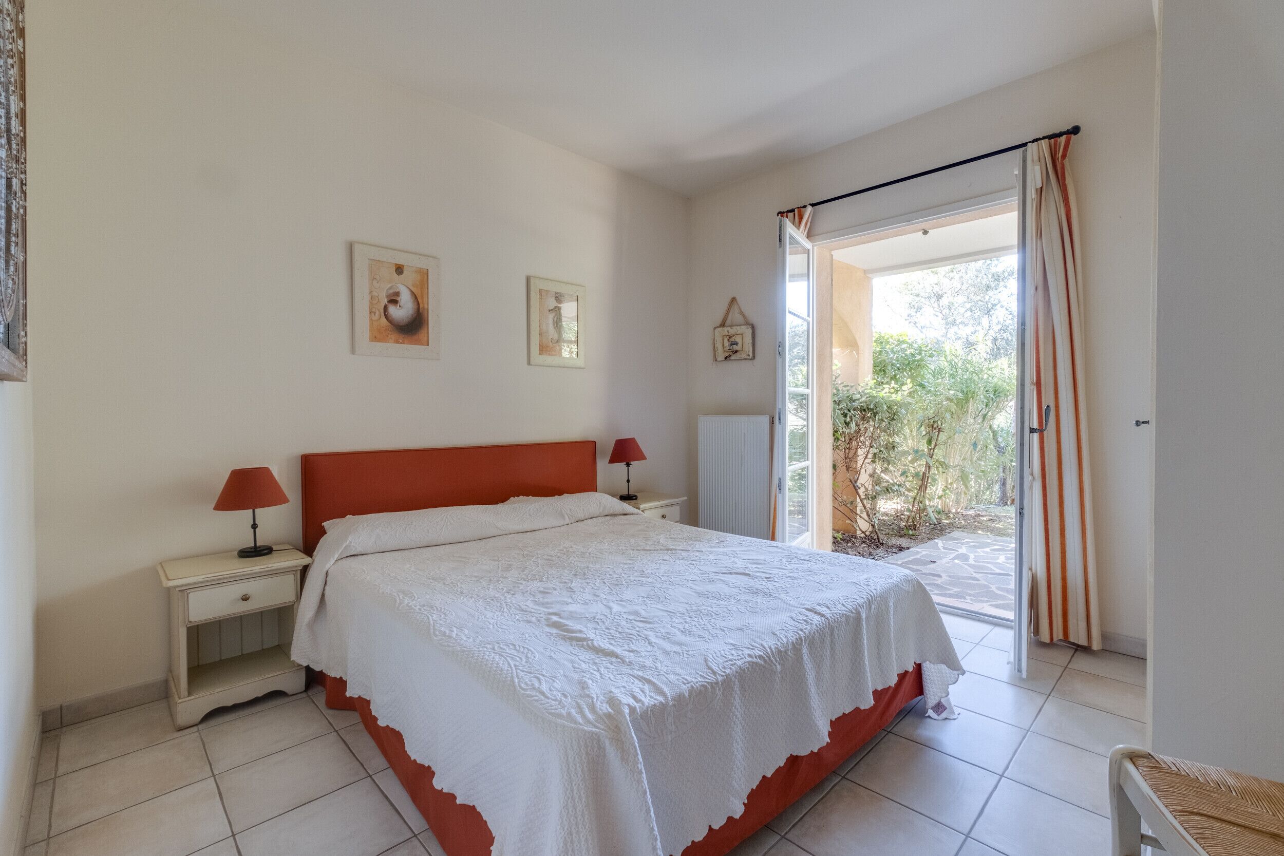 A bedroom with a bed, nightstands, and a view through an open door to an outdoor area.