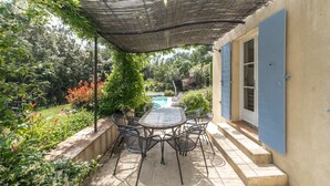 An outdoor patio with a table and chairs, surrounded by greenery and a pool in the background. - 4-BEDROOM VILLA WITH PRIVATE POOL AND GARDEN (N°442) (La Motte)