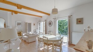 A spacious living area with a dining table, white furniture, and a large window providing natural light. - 4-BEDROOM VILLA WITH PRIVATE POOL AND GARDEN (N°442) (La Motte)