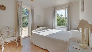 A bedroom with a bed, a chair, a table with a lamp, and a window with curtains. - 4-BEDROOM VILLA WITH PRIVATE POOL AND GARDEN (N°442) (La Motte)