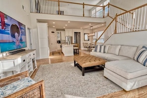 A spacious living area with a high ceiling, a staircase, a kitchen, and a television.