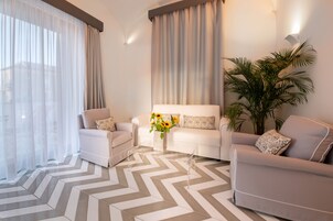 Una sala de estar moderna con dos sofás blancos, una planta grande en maceta y un suelo con estampado en forma de V.