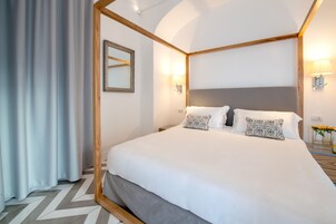 Una cama bien hecha con sábanas blancas y almohadas estampadas, un cabecero de madera y un espejo en la pared.