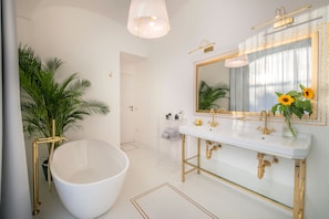 A modern bathroom with a freestanding bathtub, a large mirror with a gold frame, and a potted plant with sunflowers. - Luxury Suite with Terrace (Sant'Agnello)