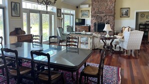 Un salon spacieux avec une grande table à manger en verre, des sièges confortables, une cheminée en pierre et un téléviseur.