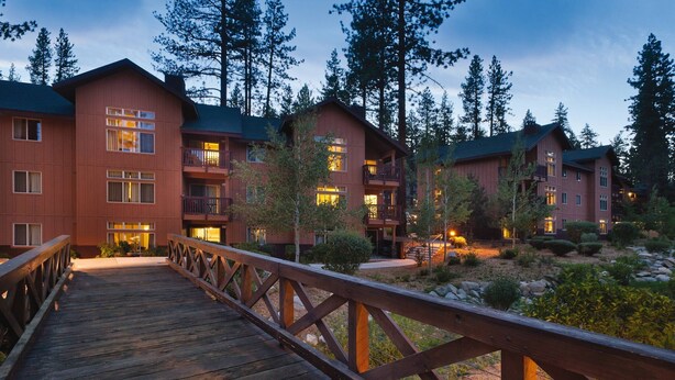 A wooden bridge leading to a row of multi-story buildings with balconies, surrounded by trees and a landscaped area. - Charming Lodge-Style Resort with Something to do in Every Season! (Zephyr Cove)